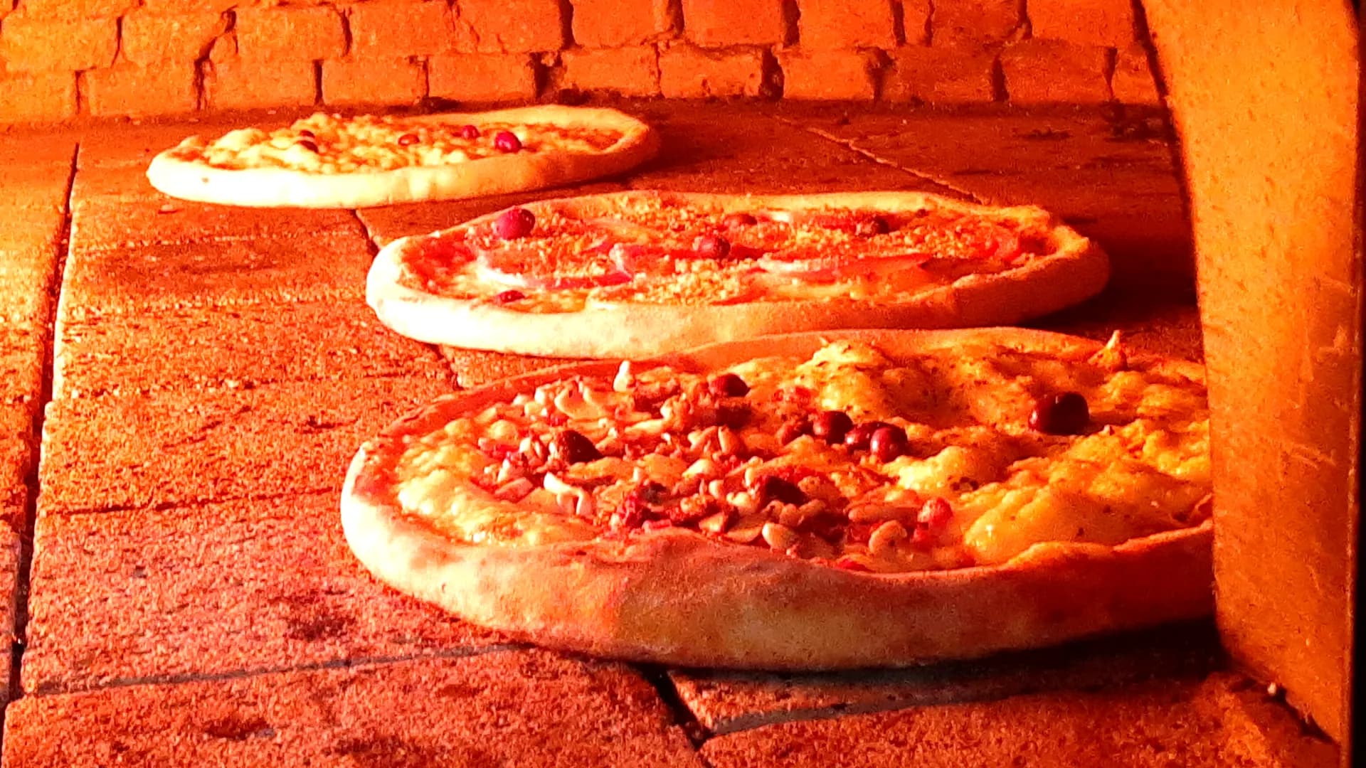 Três pizzas assando no forno a lenha da La Capanna