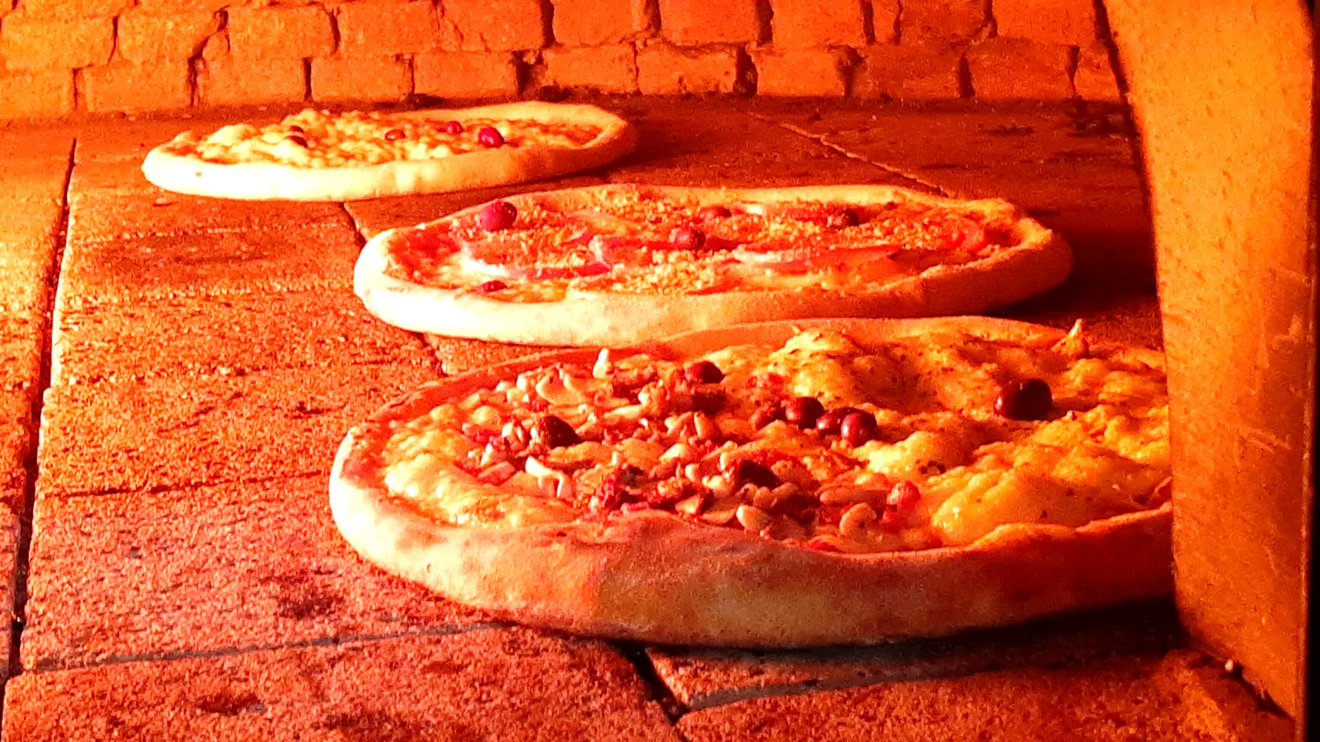Três pizzas assando no forno a lenha da La Capanna