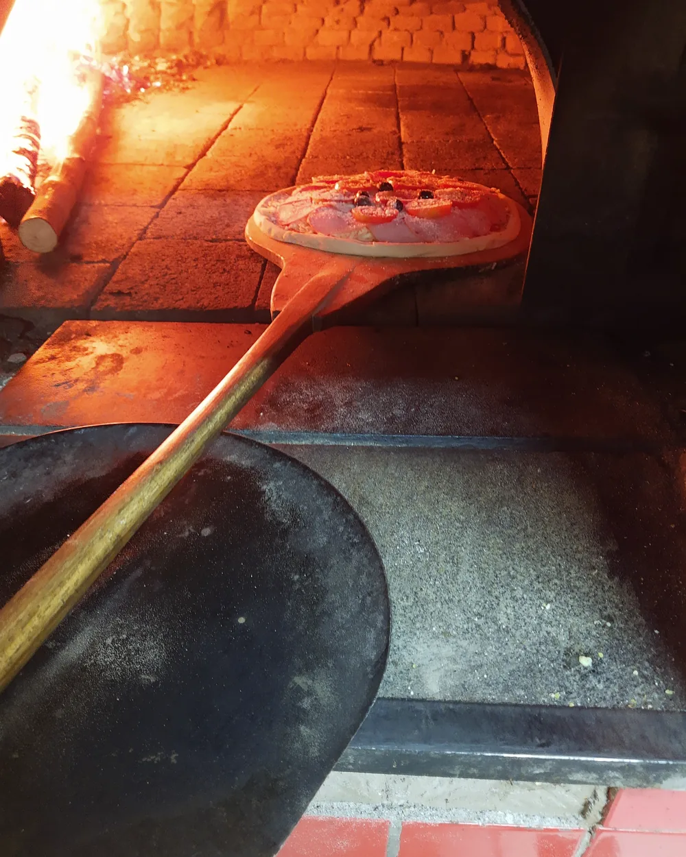 Pizza entrando no forno a lenha aceso da La Capanna